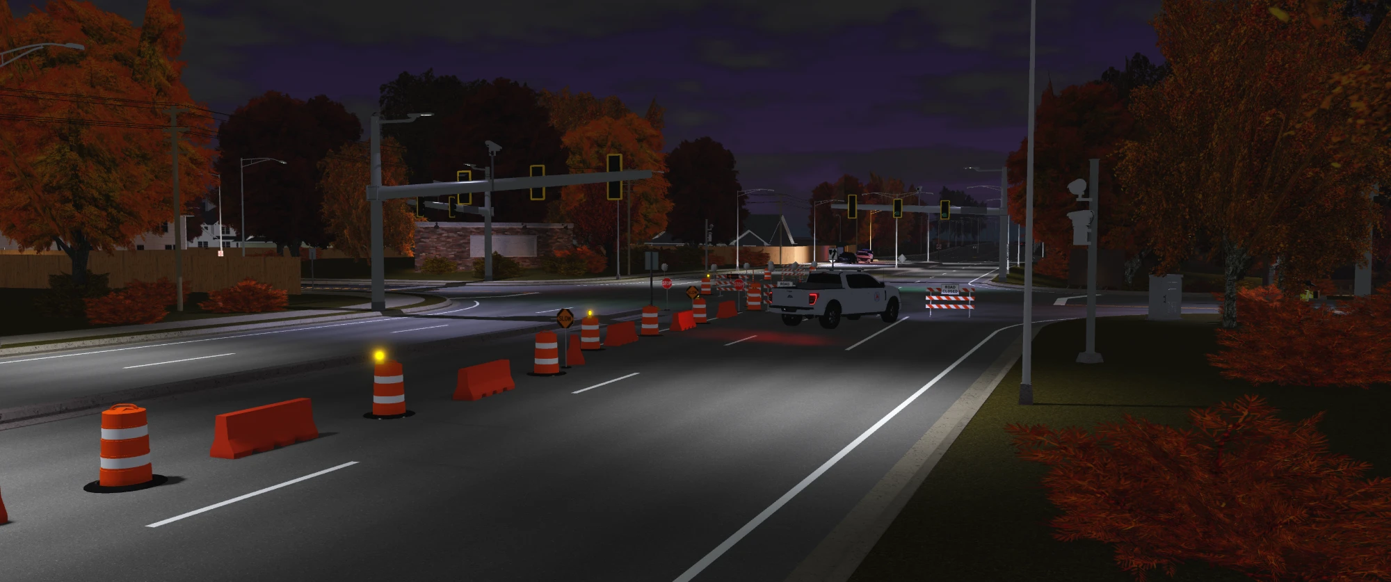 A DOT truck and barrels closing a lane at a large intersection at night.